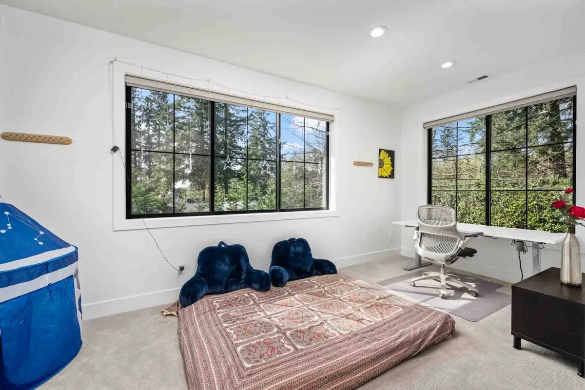A bright and inviting workspace featuring a modern desk positioned beside large windows, two plush blue chairs, and a decorative rug. The ample natural light and open view suggest a productive yet serene environment, while the calm color palette promotes focus and relaxation.