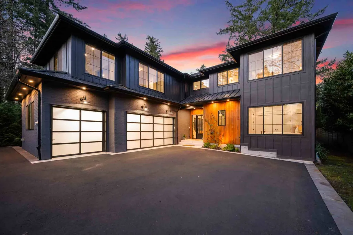 A wide shot showing the home's modern exterior with large windows, wooden accents, manicured landscaping, and a welcoming porch. The scene feels open and connected to its natural surroundings.
