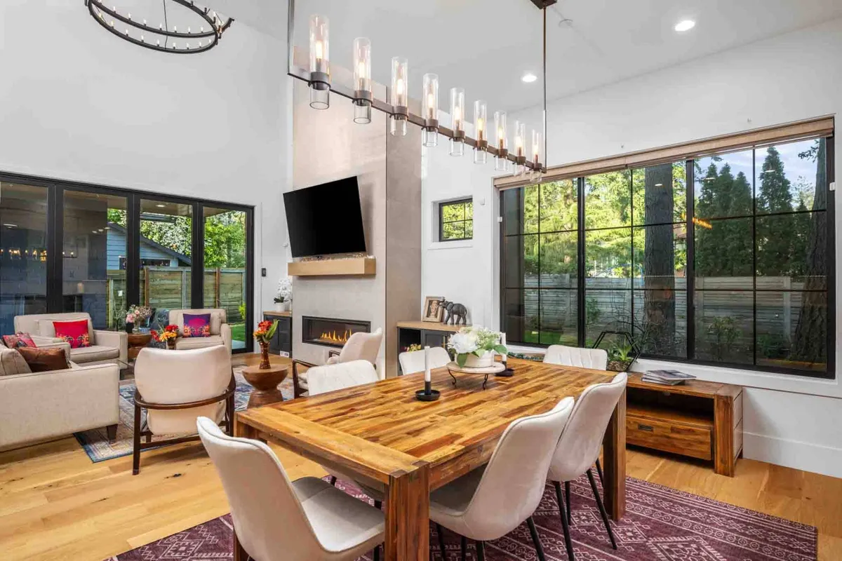 A modern, elegant dining room with a statement chandelier above a large dining table, a welcoming fireplace, and generous windows that bathe the space in natural light. The sophisticated finishes and thoughtful decor create an inviting atmosphere for special meals and shared celebrations.