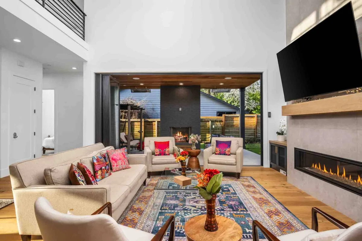 A spacious living room featuring a comfortable sofa with colorful cushions, a striking fireplace as the central focal point, a coffee table, a large TV, and a stylish rug. The decor exudes a sense of both sophistication and warmth, inviting guests to relax, socialize, and enjoy movie nights or lively conversations.