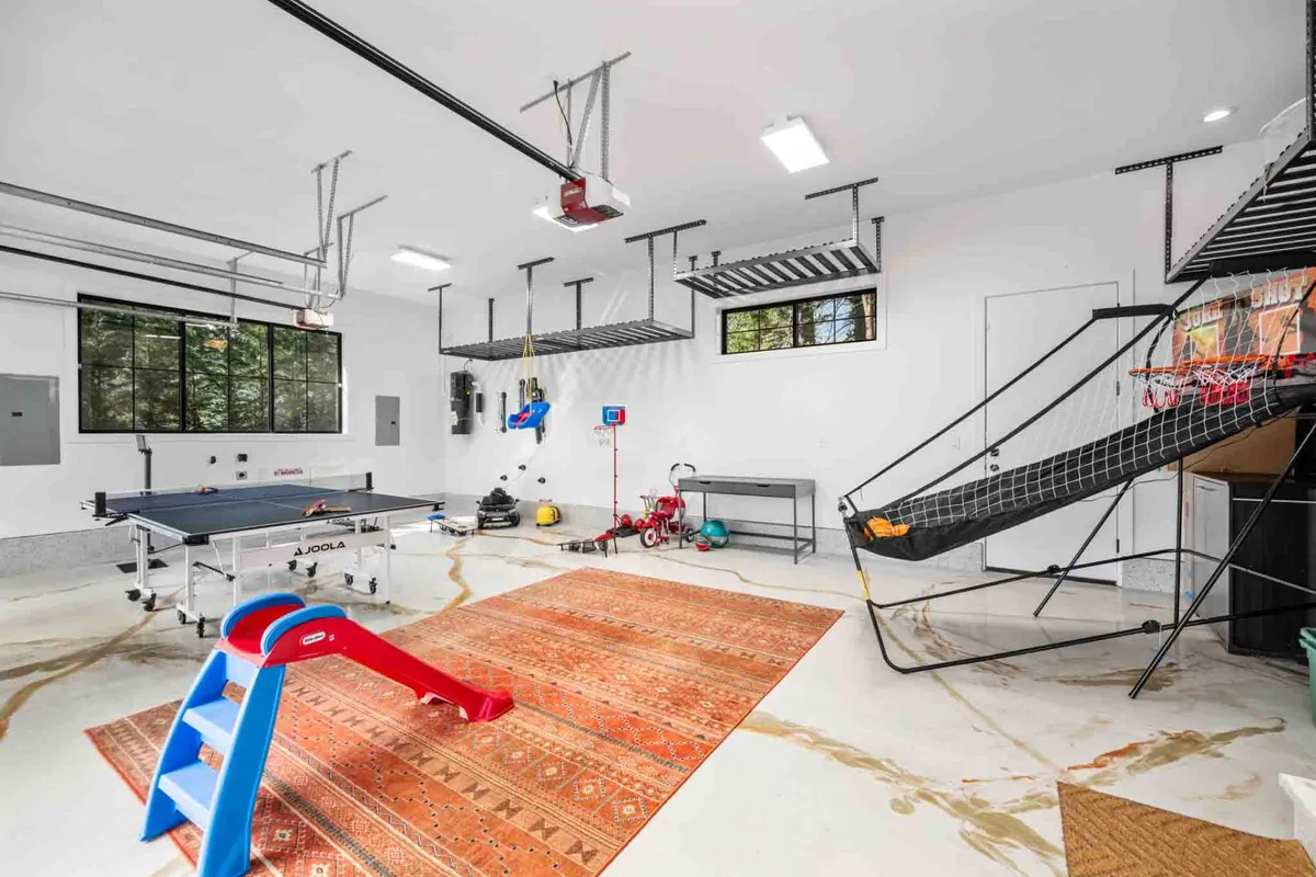 The converted garage-turned-game-room is shown here with a ping pong table, basketball hoop, toy slide, and a colorful rug. The space is alive with possibilities for play, family bonding, and energetic activities, catering to both kids and adults.