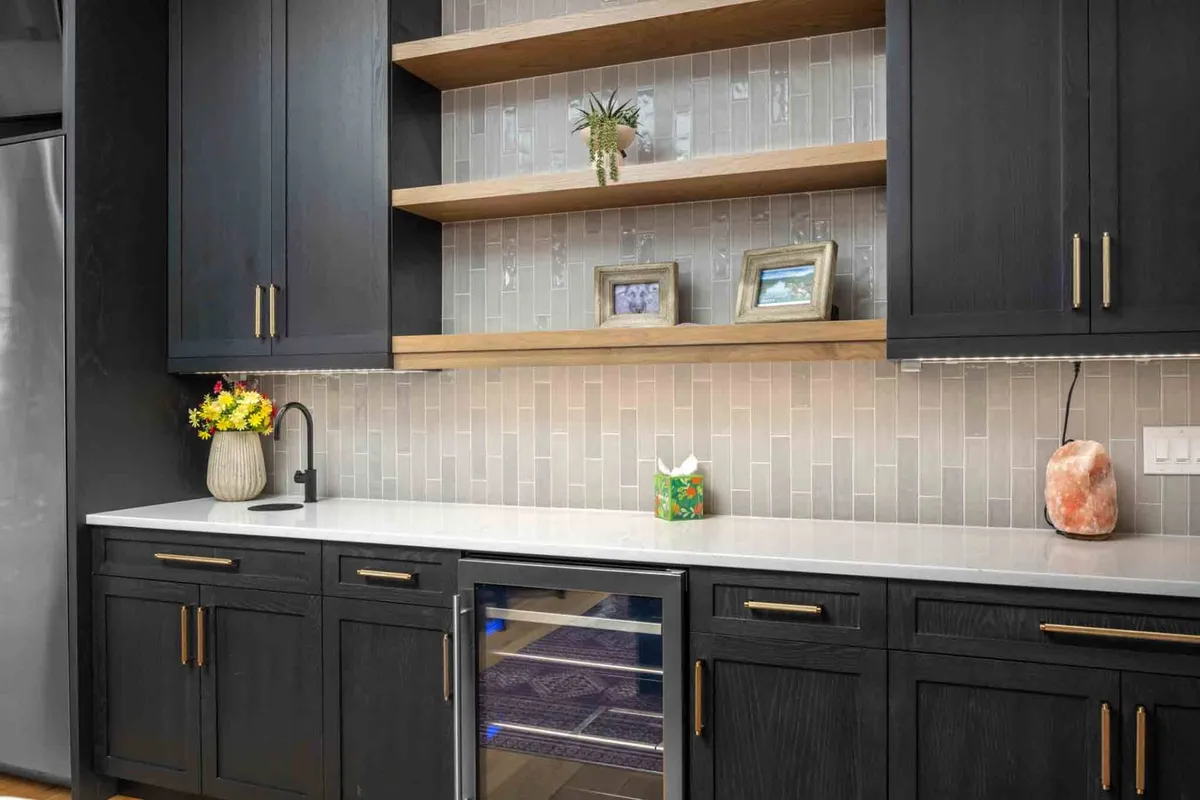 A stylish kitchen area with dark cabinetry, open shelving, countertop decor, and a mini fridge. The contemporary aesthetic and spacious layout make it ideal for hosting group dinners or informal team gatherings.