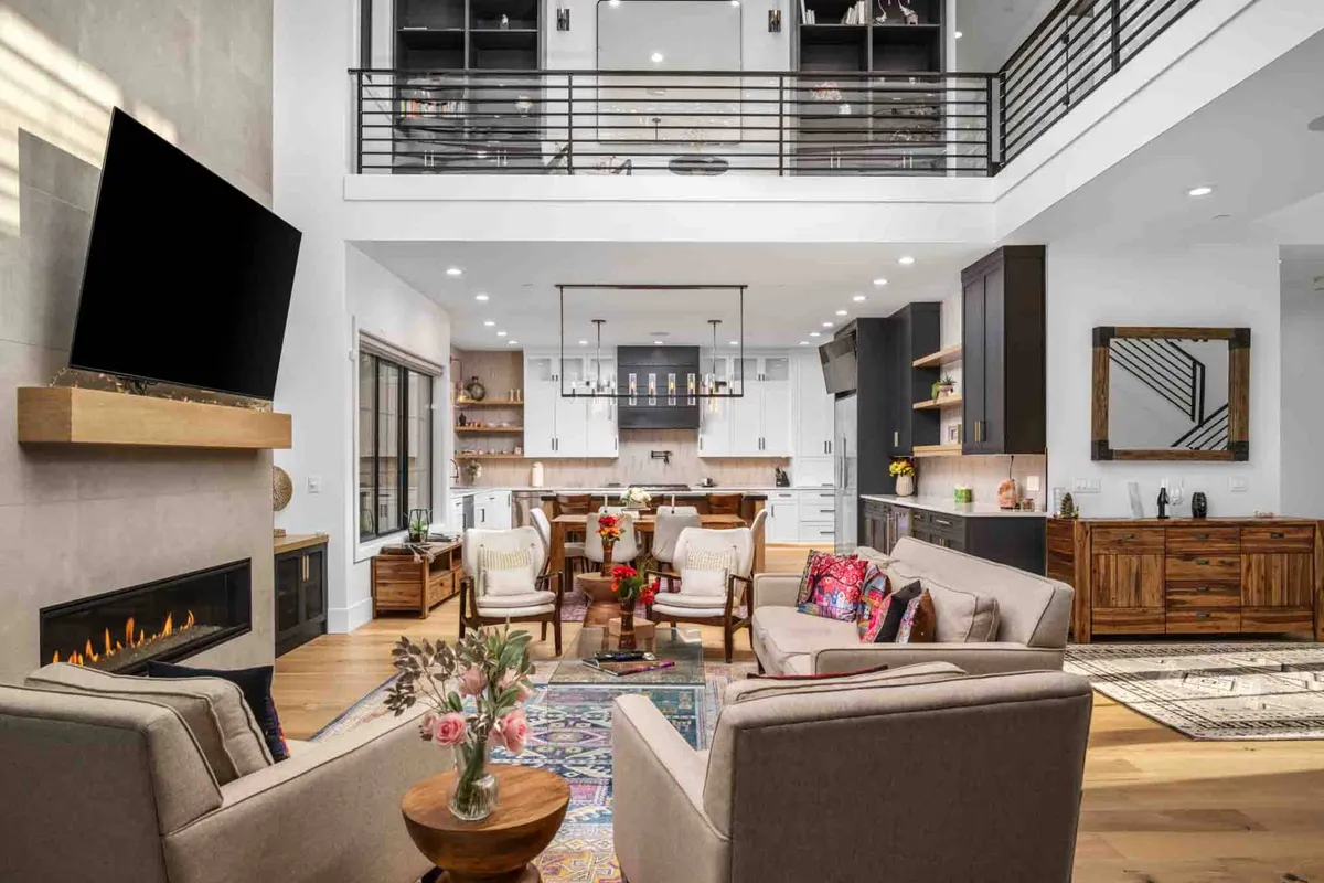 A seamless open-plan space integrating a living room with a fireplace, a kitchen island, stylish seating, a vibrant rug, and large windows. The area is filled with natural light, exuding a welcoming and sophisticated vibe—perfect for social gatherings, family meals, and relaxed evenings.