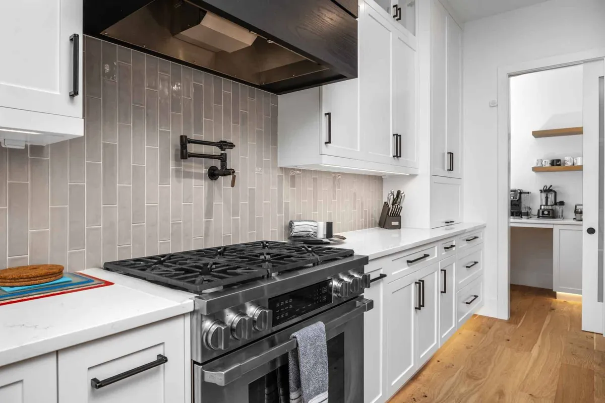 A close-up view of a kitchen workspace anchored by a stainless steel stove and modern backsplash, complemented by a sleek kitchen island. The design underscores both practicality and style, highlighting spaces for meal preparation and casual interaction.