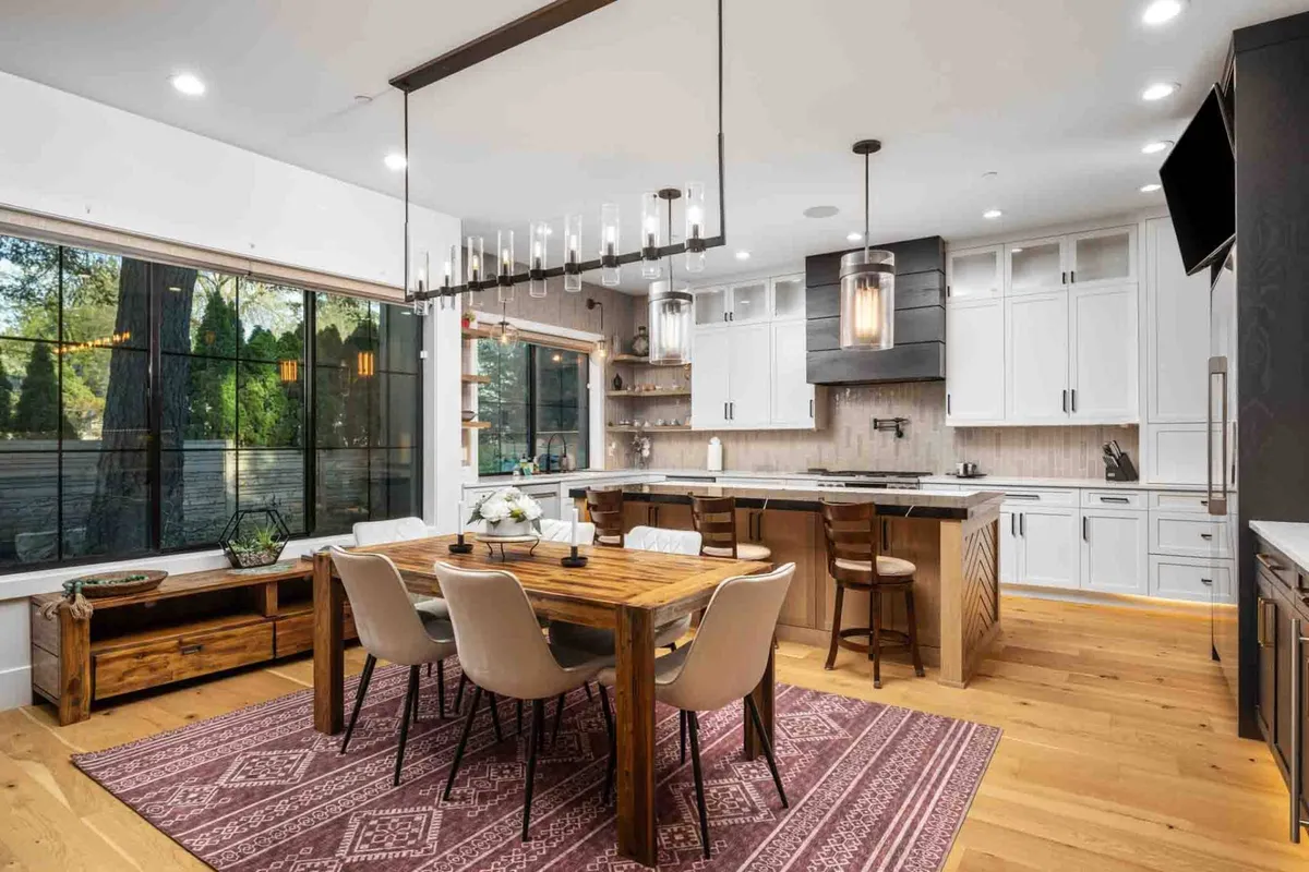 An open-concept kitchen and dining area with a large kitchen island, a welcoming dining table set near a sunlit window, and a striking chandelier. The arrangement invites both everyday meals and special occasions, seamlessly connecting preparation and entertaining spaces.