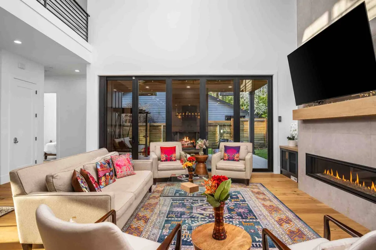 This image features a cozy sofa accented with colorful cushions, a fireplace, and large glass doors that open to the outdoors. The inclusion of a coffee table with flowers and a rug enhances the welcoming atmosphere. The seamless flow between indoors and outdoors, emphasized by the glass doors, illustrates the signature indoor/outdoor heated living area highlighted in the section.