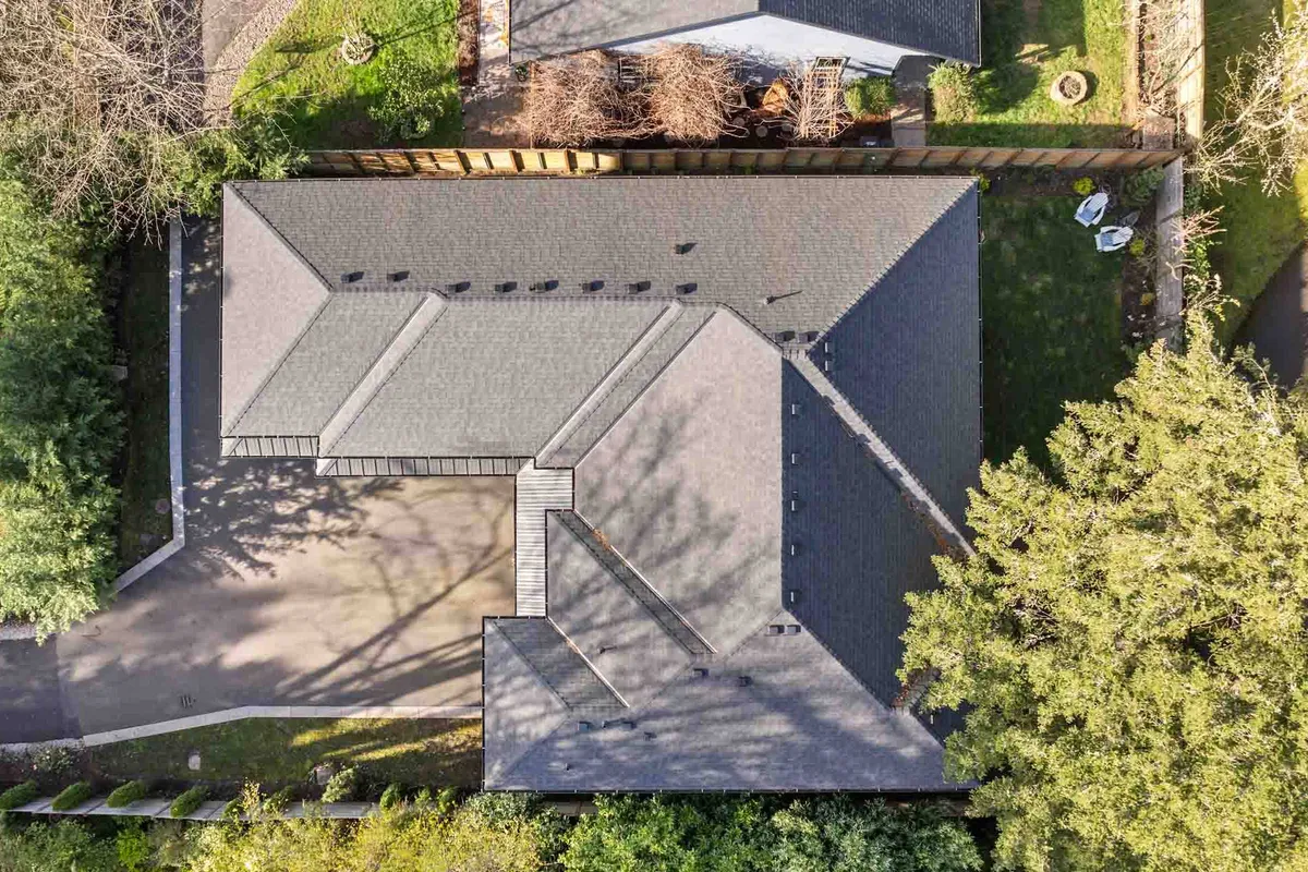 This exterior photo captures the home's roof structure set against a lush backdrop of greenery, with a spacious driveway and an inviting yard in the foreground. The surrounding trees and well-kept lawn evoke a sense of tranquility and connection to nature.